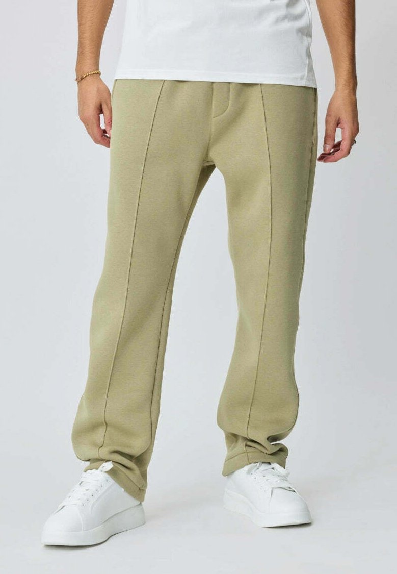 Pantalon de survêtement vert olive clair avec des détails sur les côtés, fabriqué dans un matériau doux, associé à des baskets blanches.