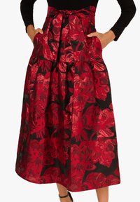 Roter Blumenkleidungsrock mit schwarzem Hintergrund, aus einem strukturierten Stoff gefertigt. Er hat einen bindbaren Taillenbund und Taschen, mit einem bodenlangen Design.