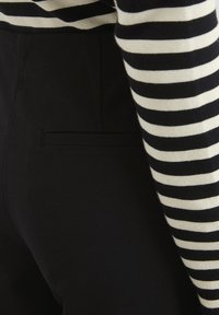 Zwarte stoffen broek met een vlakke achterzakdetail. Gecombineerd met een gestreepte zwart en crèmekleurige lange mouwen top die een gebreide textuur toont.