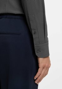 Svartvitrandig prickig skjorta med knäppmanschett, kombinerad med marinblå texturerade byxor med en slät sidoficka.