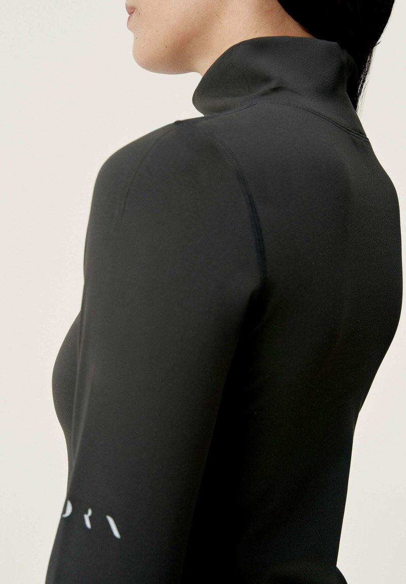Czarny top z długim rękawem i wysokim kołnierzem, o dopasowanym kroju i gładkiej fakturze. Warto zwrócić uwagę na subtelną logo na rękawie.