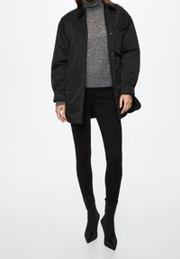 Zwarte geïsoleerde jas met knopen en een aansluitende grijze coltrui en zwarte leggings, afgemaakt met puntige enkellaarsjes.