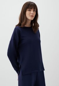 Granatowa bluzka z długim rękawem, okrągłym dekoltem, opadającymi ramionami i szczelinami po bokach. Miękka tkanina o gładkiej strukturze i luźnym kroju.