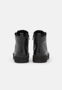 Botas de tobillo de cuero negro con un cuello forrado de piel, textura suave y cierres de cremallera. La suela presenta estrías horizontales para mayor agarre.