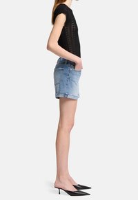 Czarny, dziany top z krótkimi rękawami, o teksturowanym wzorze; jasnoniebieskie szorty dżinsowe z postrzępionym dołem; czarne szpilki z zaostrzonym noskiem. Widok z boku.