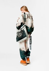 Chaqueta extragrande con estampado de montaña, detalles en negro, combinada con pantalones jogger a juego. Botas naranjas con suela de goma, bolso bandolera con detalles gráficos.