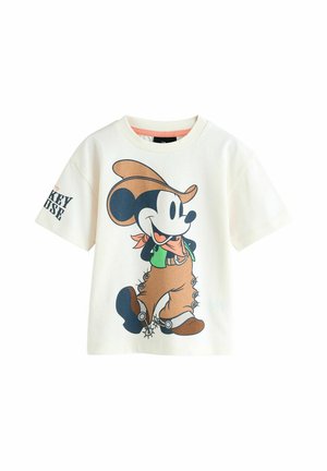 T-shirt en coton blanc avec un cartoon d'un personnage souriant en tenue de cowboy, avec des accents verts et des boutons noirs sur un pantalon marron.