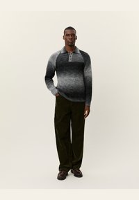 Pulover tricotat cu gradient în gri și negru, cu guler și trei butoane, asortat cu pantaloni din catifea engleză verde închis și pantofi maro.
