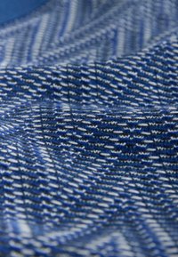 Gros plan sur un tissu bleu texturé avec des rayures tissées blanches et noires formant un motif diagonal et des détails en relief.