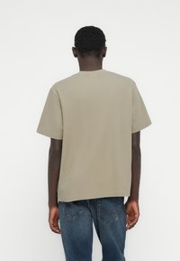 Κοντομάνικο, ριμπ μπλουζάκι σε χακί πράσινο, με στρογγυλή λαιμόκοψη και χαλαρή εφαρμογή. Συνδυασμένο με μπλε τζιν, εμφανίζεται από την πίσω όψη.