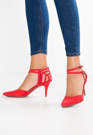 Røde ruskindssko med høje hæle, spidse tæer, ankelremme og udskåret detaljer. Hælene har en slank, stilethæl-form.