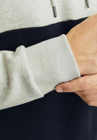 Sudadera bloqueada en gris y marino que presenta un puño acanalado, textura suave y cordón ajustable en el cuello.