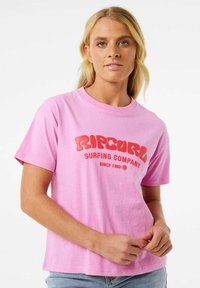 Roze katoenen t-shirt met een opvallend rood logo van "Ripcurl Surfing Company" in ronde letters. Korte mouwen en een comfortabele pasvorm.