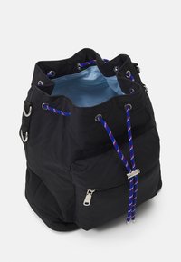 Czarna nylonowa torba w kształcie wiadra z systemem ściągacza, z niebieskim, czerwonym i białym sznurkiem, zapinaną na zamek przednią kieszenią oraz jasnoniebieską podszewką.