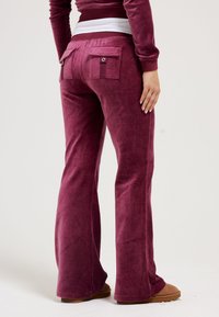 Burgundy flared pants made of soft velour with two back pockets, textured fabric, and a wide waistband that features a contrasting band.
