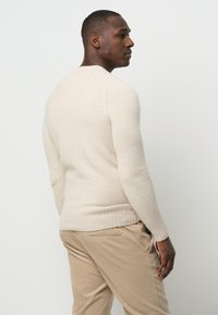 Cremefarbenes Strickpullover mit Rundhalsausschnitt, langen Ärmeln und geripptem Saum. Weiche Textur und figurnaher Schnitt.