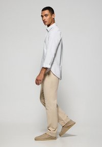 Camicia bianca a righe con maniche arrotolate, pantaloni beige e espadrillas chiare. Design semplice e sartoriale con colori neutri.