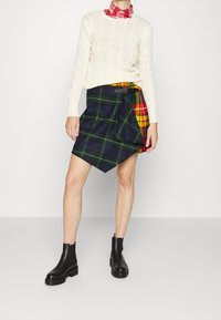 Mjölnad krämfärgad tröja, rutigt omslagskjol i marinblått, grönt och rött, med bälte i midjan. Svarta ankelstövlar med tjocka sulor.