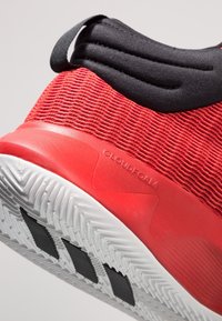Chaussure de sport rouge avec dessus en tissu texturé, accents noirs et semelle en caoutchouc présentant un motif de bande de roulement en zigzag. "CLOUDFOAM" moulé près du talon.