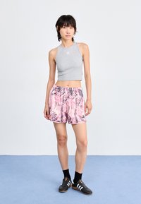 Športový outfit pozostávajúci z šedej skrátenej tielka a ružových šortiek s vzorom a čiernym logom. Čierne ponožky a topánky dotvárajú vzhľad.