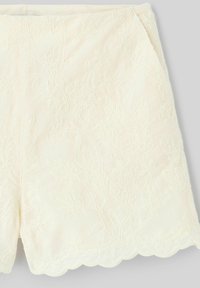 Jupe couleur crème avec motifs floraux en relief, ourlet festonné et taille lisse, présentée à plat.