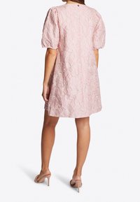 Różowa sukienka z teksturowym kwiatowym wzorem, krótkimi bufkami i luźnym krojem, sięgająca tuż nad kolana, w połączeniu z cielistymi sandałami na obcasie.