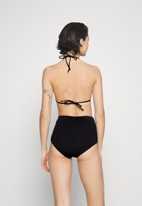Svart bikini med halterneck och knytstängning, med hög midja och texturerade underdelar. Slät tyg med minimal detaljer.