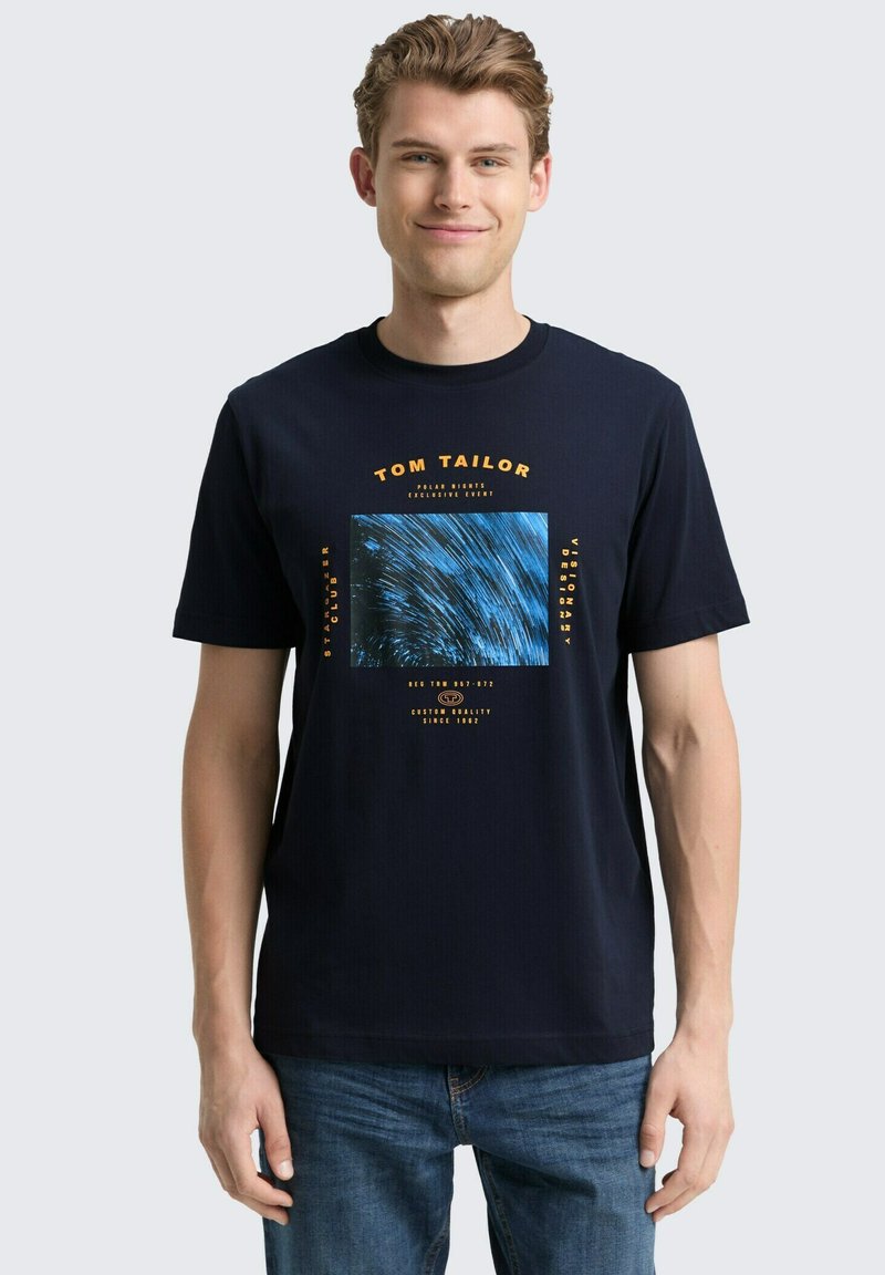 Granatowa koszulka z krótkim rękawem, wykonana z bawełny, z centralnym wzorem graficznym w postaci niebieskich spiral oraz pomarańczowych akcentów tekstowych.