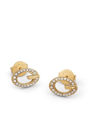 Boucles d’oreilles clous Guess dorées en forme de lettre G, chacune ornée d’une rangée de cristaux ronds transparents.
