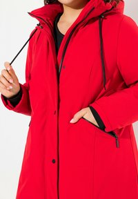Red jacket with a zipper front and hood. It features black accents, two zippered side pockets, and a smooth, textured fabric.