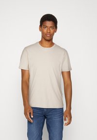 Tricou bej cu mânecă scurtă, dintr-un material moale și texturat, cu un guler rotund și o croială normală, asociat cu blugi albaștri.