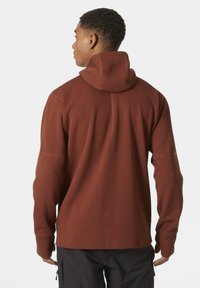 Sudadera roja con textura, de cuello alto y mangas ajustadas, que incluye una capucha ceñida. Combinada con pantalones oscuros, mostrando un ajuste cómodo.