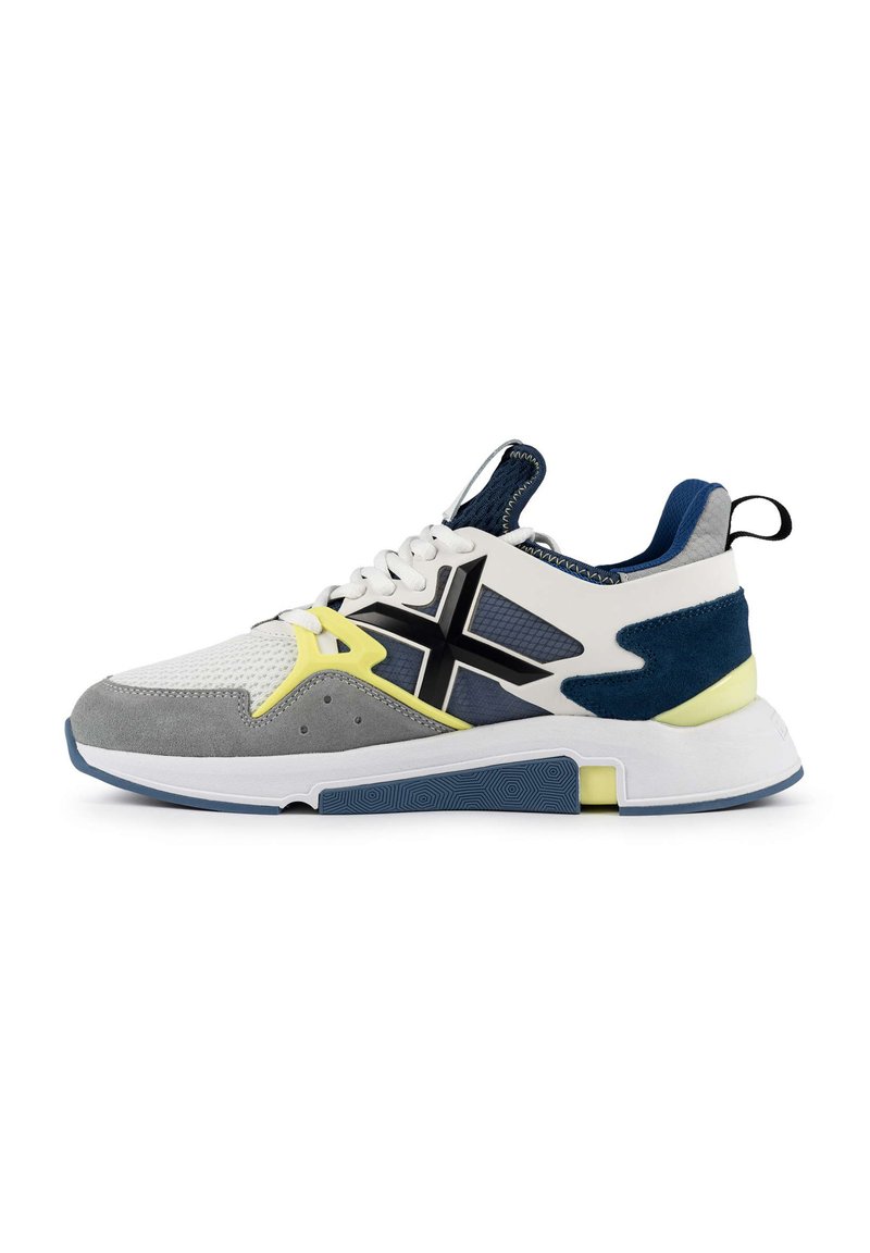 Basket de sport en blanc, gris et bleu marine avec une tige en maille, des accents en daim, une semelle texturée et des détails en jaune vif.