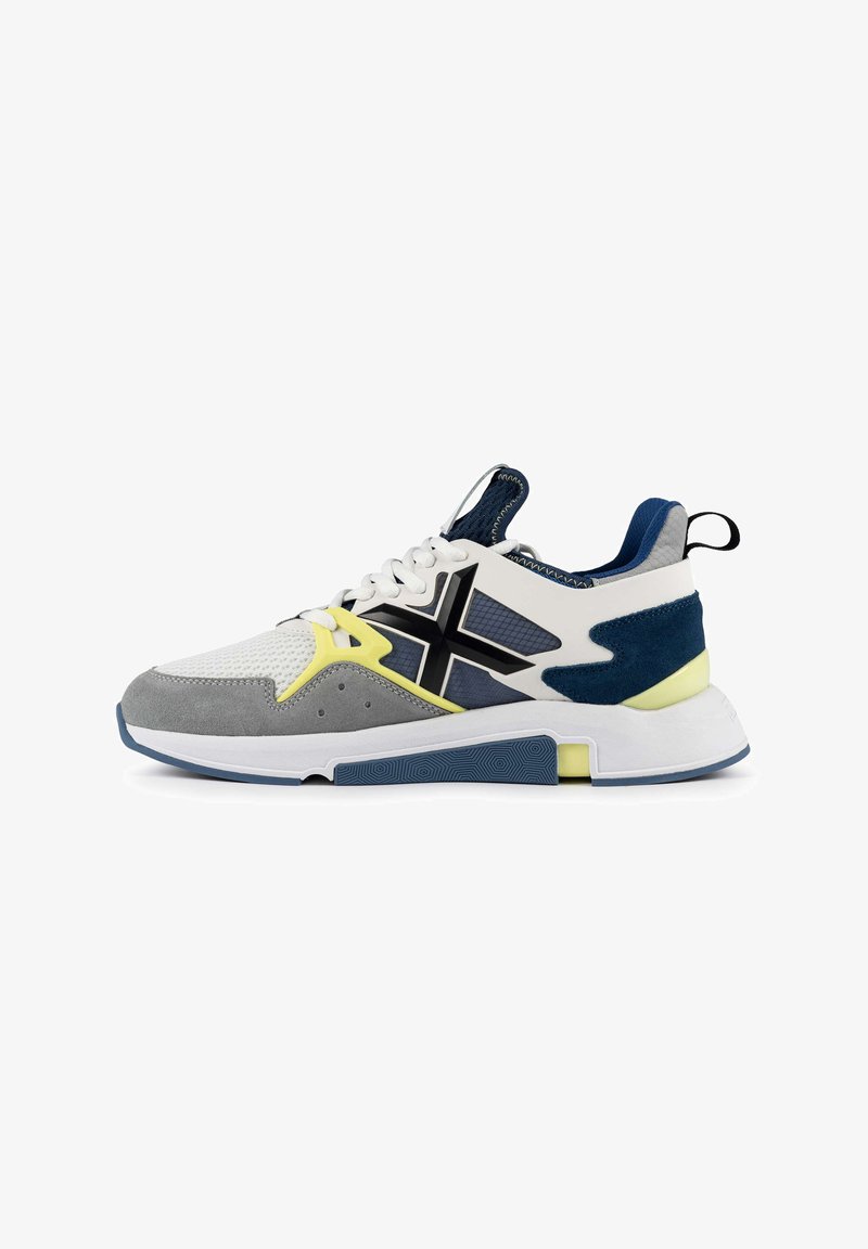 Basket de sport en blanc, gris et bleu marine avec une tige en maille, des accents en daim, une semelle texturée et des détails en jaune vif.