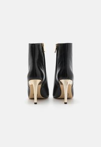 Mustad nailonööriga mustad nahksandaalid, millel on kõrged kuldsed stiletto kontsad ja külgsiibrit, omades sujuvat, sileda viimistluse ja ümarat varvata.