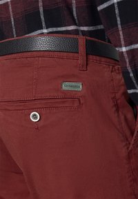 Bordeauxfärgade byxor med en bakficka och knapp, kompletterade med ett texturerat svart bälte och en svart-och-röd rutig skjorta.