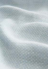 Tissu tissé bleu clair avec un motif texturé subtil, présenté en plis doux et en détail rapproché.