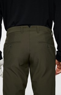 Oliwkowe spodnie o dopasowanym kroju, z tylnymi kieszeniami zapinanymi na guziki oraz delikatną teksturą. W zestawie z czarną koszulą z długim rękawem.