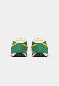 Zelene i žute atletske cipele od suede materijala, s bijelim oznakom na peti i teksturiranom gumenom podlogom. "Reebok" logo na peti.