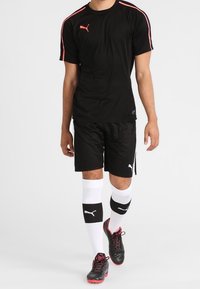 Camiseta atlética negra con rayas rosas, pantalones cortos negros a juego, calcetines blancos y negros, y zapatos de fútbol negros con acentos rosas.