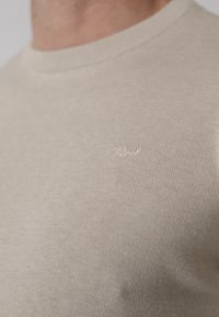 Maglione beige a girocollo realizzato in morbido tessuto a maglia fine, con una sottile texture e un piccolo logo ricamato sul davanti.