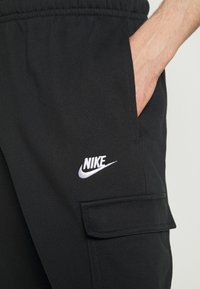 Svarta joggerbyxor i mjukt tyg med elastiskt midjeband, sidofickor och en vit Nike-logotyp broderad på framsidan.