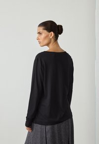 Czarna koszula z długim rękawem, wykonana z miękkiego materiału, z szerokim dekoltem w serek i luźnym krojem, zestawiona z połyskującą szarą spódnicą midi.