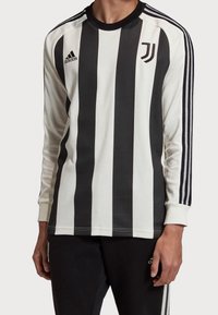 Langærmet trøje i sort og hvid strib, med Juventus-logoet og tre sorte striber ned langs ærmerne. Fremstillet af tekstureret stof.