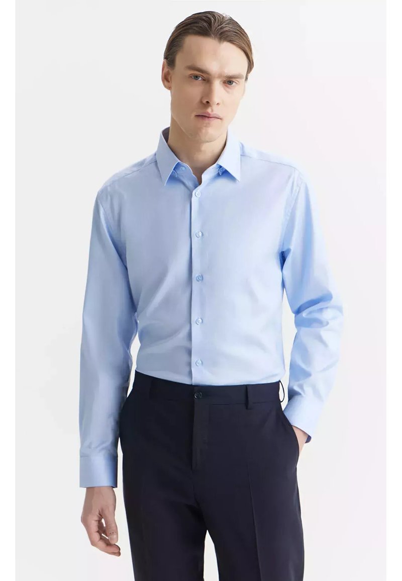 Jasnoniebieska koszula zapinana na guziki, wykonana z gładkiego materiału, z klasycznym kołnierzykiem, długimi rękawami i dopasowanym krojem, w połączeniu z ciemnymi spodniami.