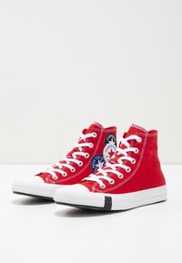 Sneakers alti rossi in tela con lacci bianchi, punta in gomma e accenti neri. Presentano un'etichetta circolare con logo sul lato.