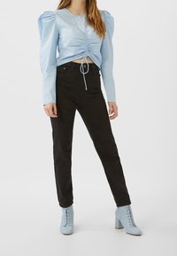 Blusa de manga abullonada en azul claro con frente fruncido, combinada con jeans ajustados negros y botas de tobillo de encaje azul claro.
