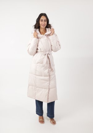 Gevoerde jas in lichtroze, met een hoge kraag en riem, met gestikte secties en een zachte textuur. Gecombineerd met denim en transparante blockhakken.