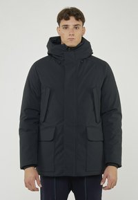 Parka isolante di colore blu navy con cappuccio, dotata di due tasche frontali e una cerniera frontale. Texture liscia con elementi di design minimali.