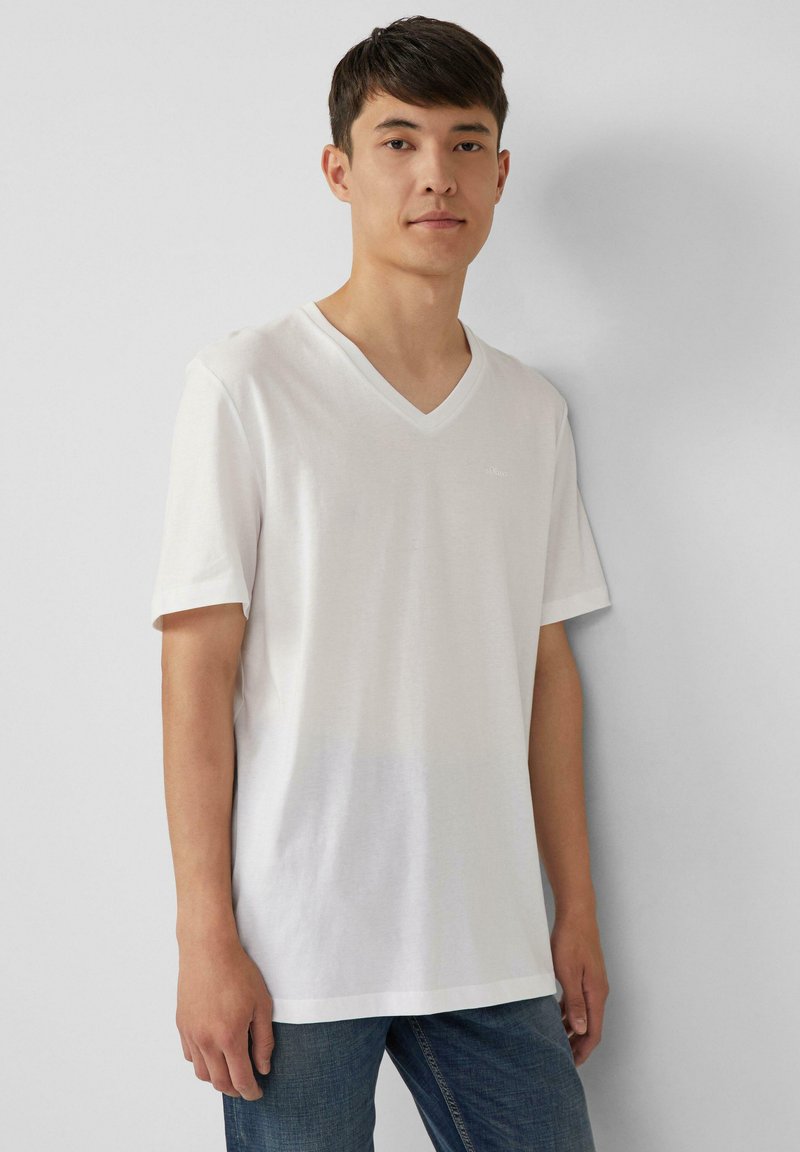 Witte V-hals t-shirt gemaakt van gladde katoenstof, met korte mouwen en een ontspannen pasvorm, gedragen met donkerblauwe jeans.